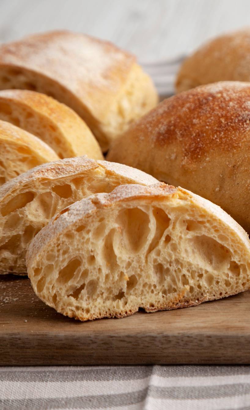 Drei selbstgebackene Ciabatta-Brote mit Trockenhefe auf einem Holzbrett, eines davon in Scheiben geschnitten