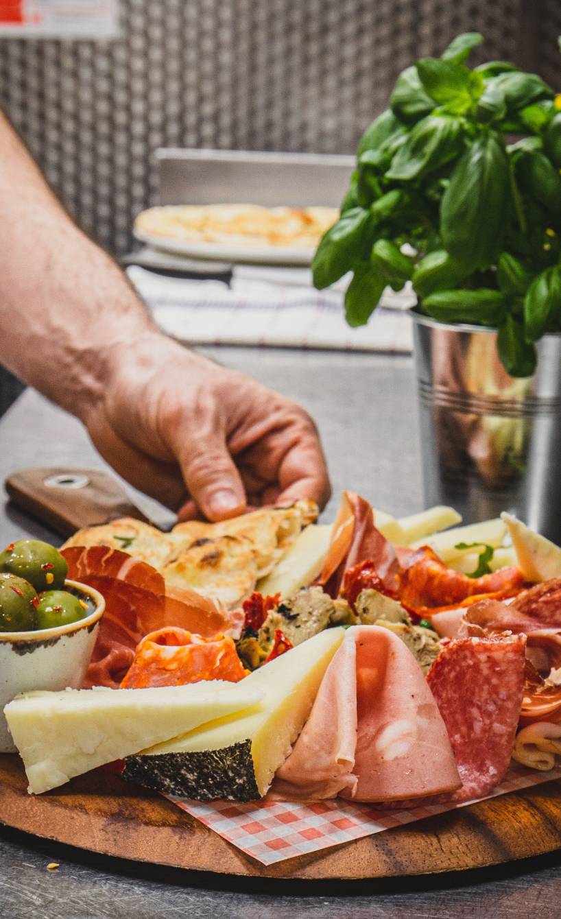 Ein Mann richtet verschiedene italienische Antipasti auf einem runden Holzbrett an