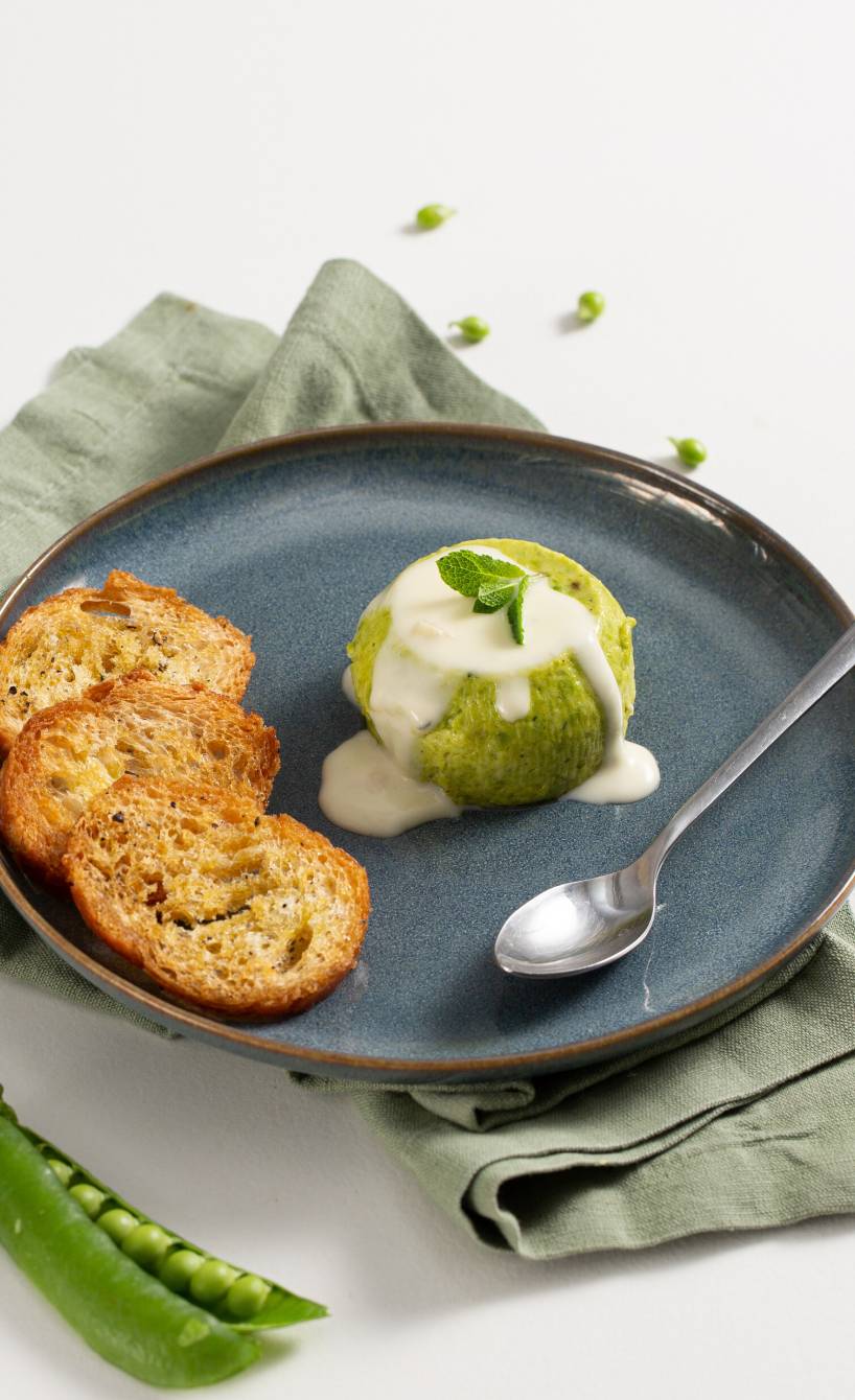 Eine Portion italienischer Erbsenflan übergossen mit Parmesansauce angerichtet mit gerösteten Brotscheiben auf einem Vorspeisenteller