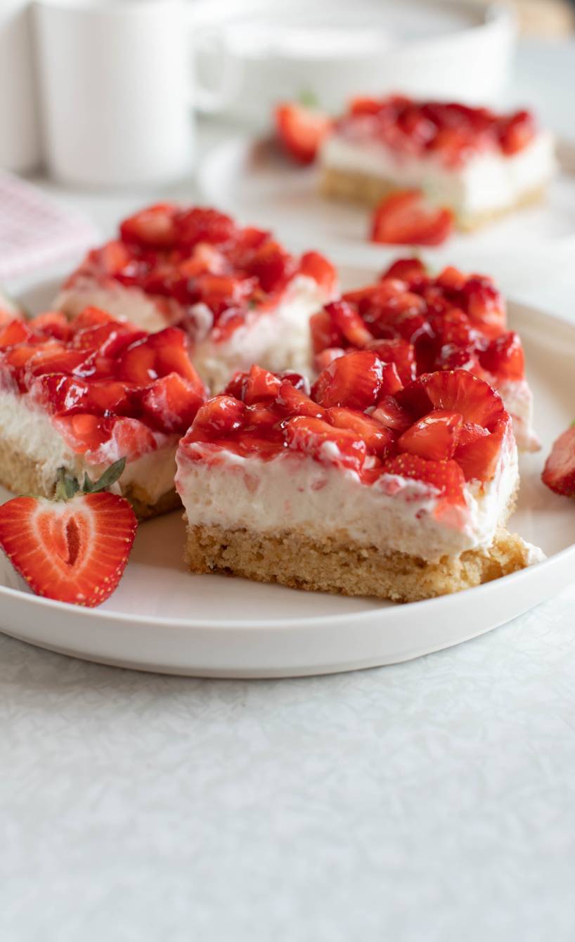 Mehrere Stücke selbstgebackener Blechkuchen mit Erdbeeren und Pudding-Quark-Creme auf einem Kaffeetisch