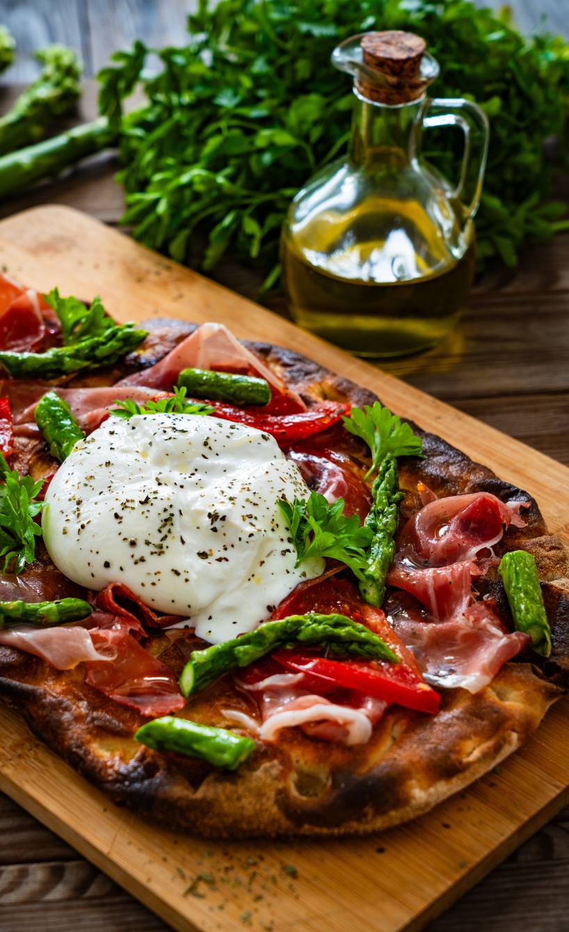 Selbstgebackene Pinsa belegt mit grünem Spargel, Schinken und Burrata auf einem Holzbrett