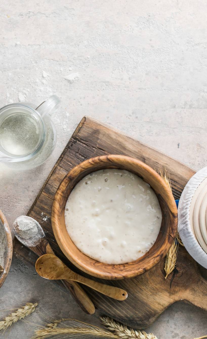 Aktiver Sauerteigstarter auf einem Tisch neben weiteren Brotbackzutaten wie Mehl und Wasser