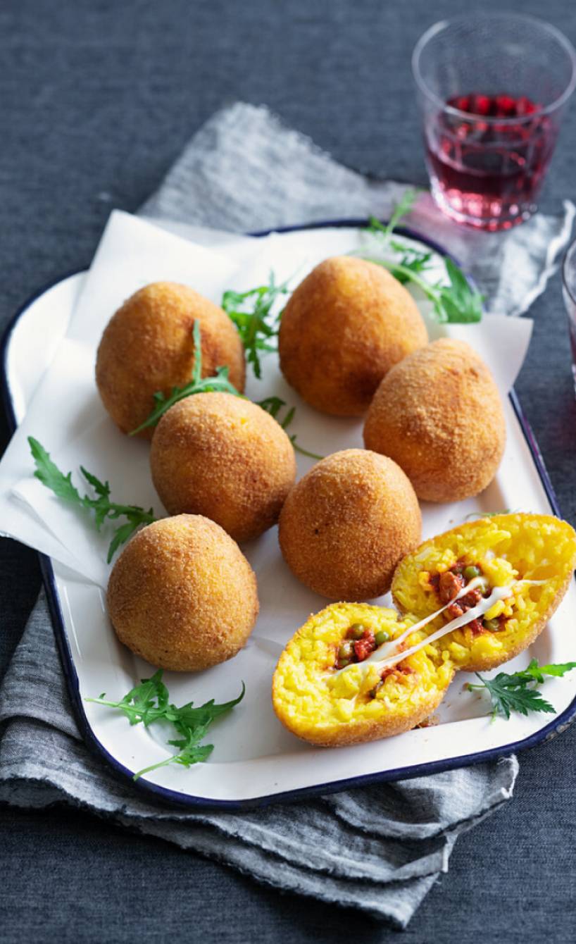 Mehrere selbstgemachte Arancini mit Safran und Ragù-Füllung, teilweise angeschnitten auf einer Servierplatte