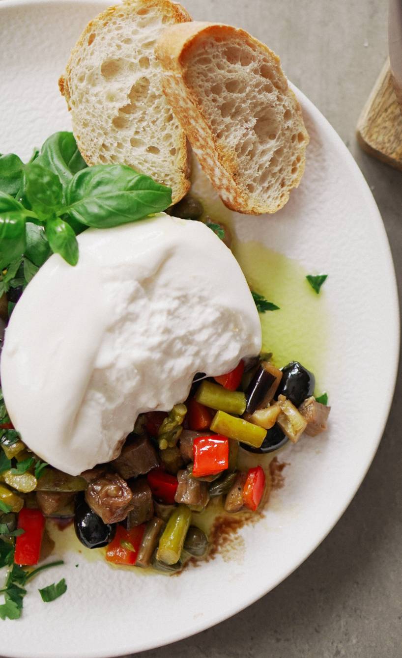 Caponata mit grünem Spargel und Burrata auf einem Vorspeisenteller, daneben Ciabartta-Scheiben
