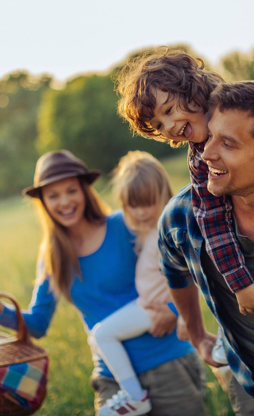 Eine Familie läuft lachend über ein Feld, die Mutter trägt einen Picknickkorb
