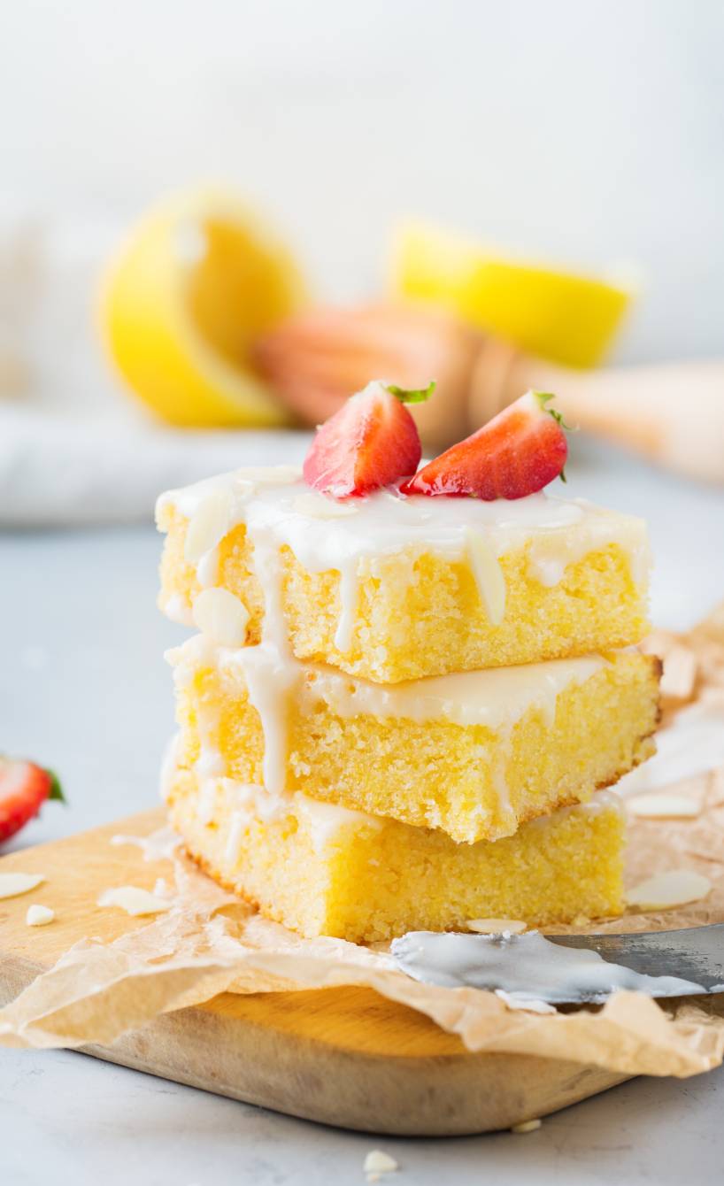 Drei Stücke Polenta-Zitronen-Blechkuchen gestapelt und getoppt von frischen Erdbeeren auf einem Kuchenteller Drei Stücke Polenta-Zitronen-Blechkuchen gestapelt und getoppt von frischen Erdbeeren auf einem Kuchenteller