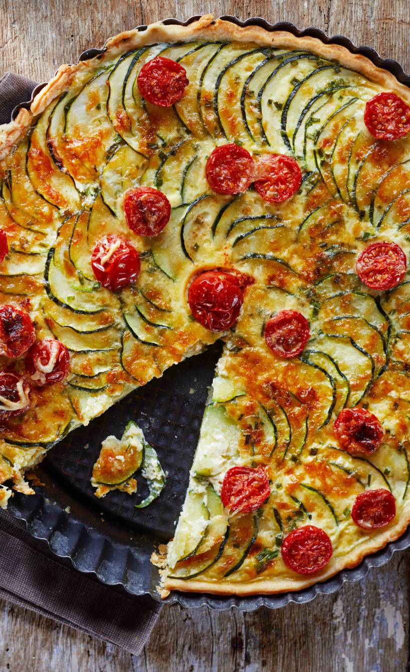 Selbstgebackene Zucchini-Quiche mit Mürbeteig-Boden, Tomaten und Käse angeschnitten auf einem Tisch