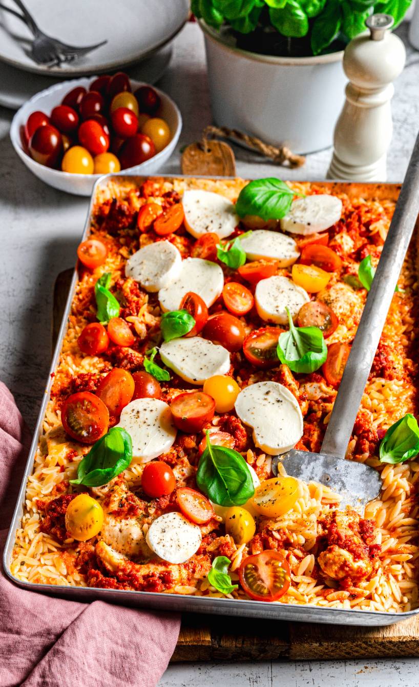 Ein Blech mit gebackenen Risoni, Hähnchen, Tomate und Mozzarella garniert mit Basilikum auf einem Tisch