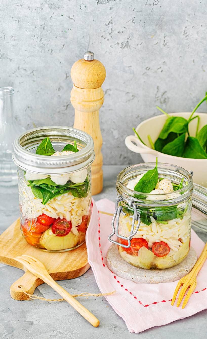 Italienischer Schichtsalat in zwei Weckgläsern mit Risoni, Tomaten, Mozzarella, Artischocken und Dressing