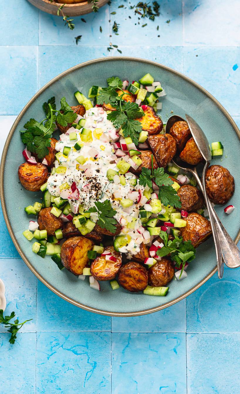Röstkartoffelsalat mit Gurke und Radieschen getoppt von Joghurt-Dip auf einem tiefen Teller