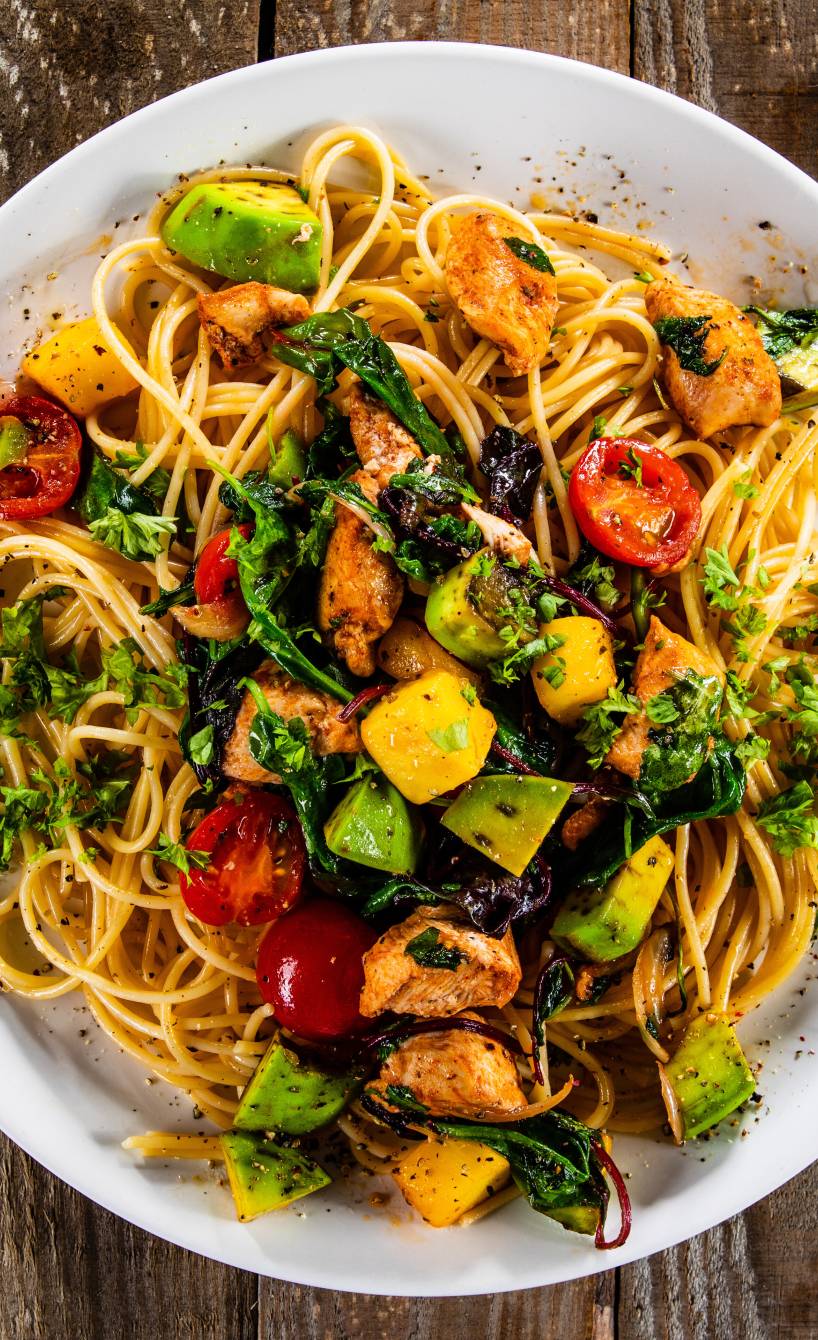 Spaghetti "Tropicana" mit gebratenen Hähnchenbrustfiletstücken und Würfeln von Avocado und Mango angerichtet auf einem Pastateller mit frischen Kräutern