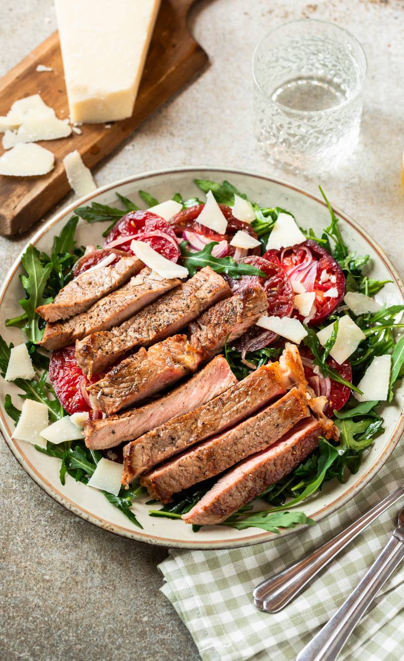 Gebratene Rumpsteak-Streifen Tagliata di manzo auf mit Rucola-Tomaten-Salat getoppt von Parmesanspänen auf einem tiefen Teller