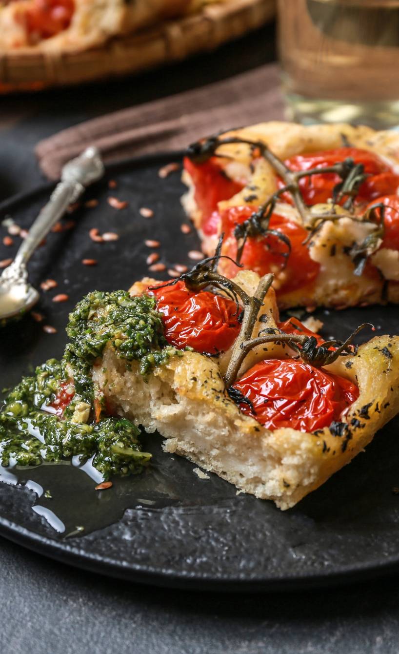 Selbstgebackene Focacciastücke belegt mit Kirschtomaten, daneben grünes Pesto als Dip