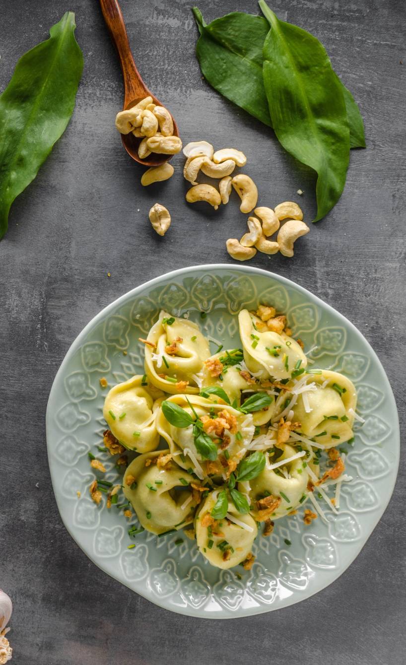 Selbstgemachte Tortellini mit verschiedenen Zutaten für Füllungen daneben auf einem Tisch