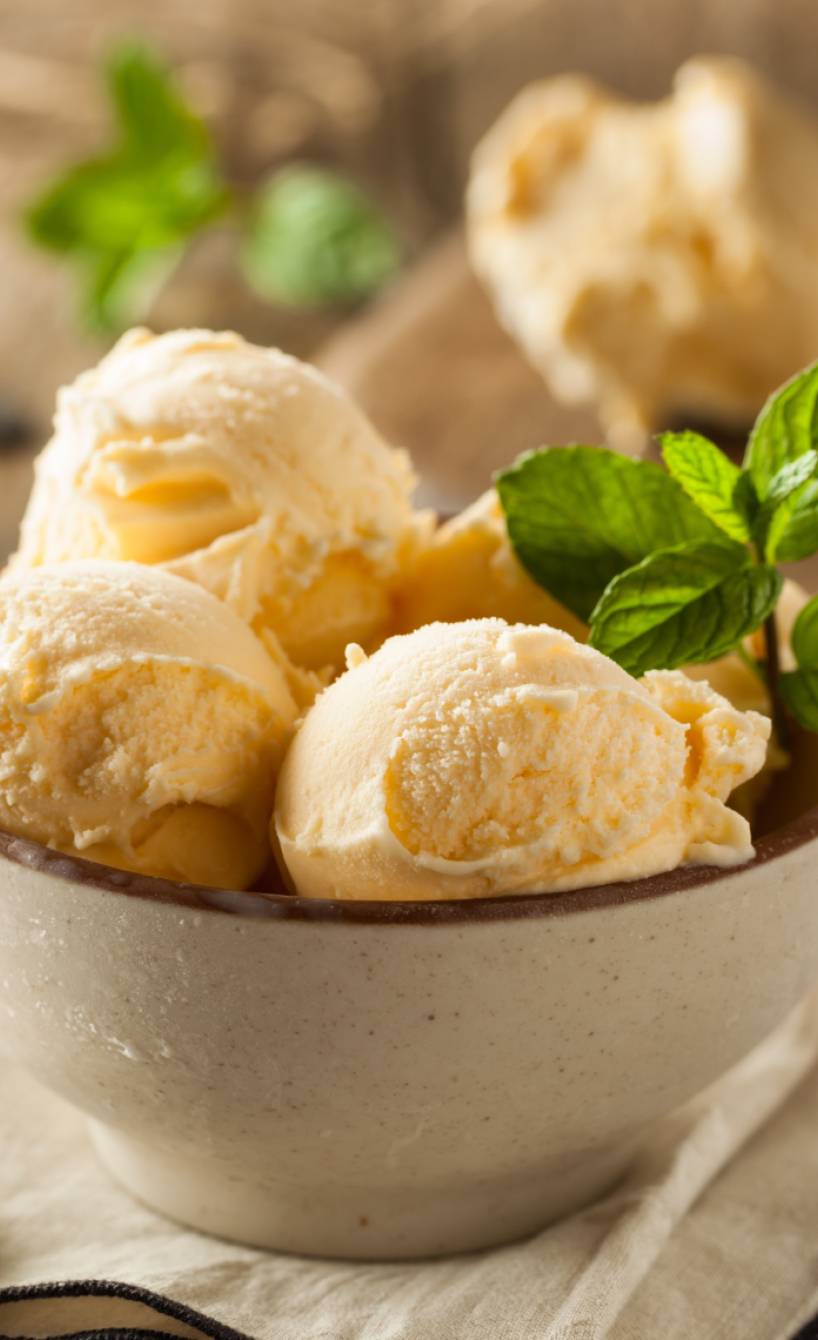 Mehrere Dessertschalen mit Vanilleeis-Kugeln garniert mit frischen Minzblättern auf einem Holztisch