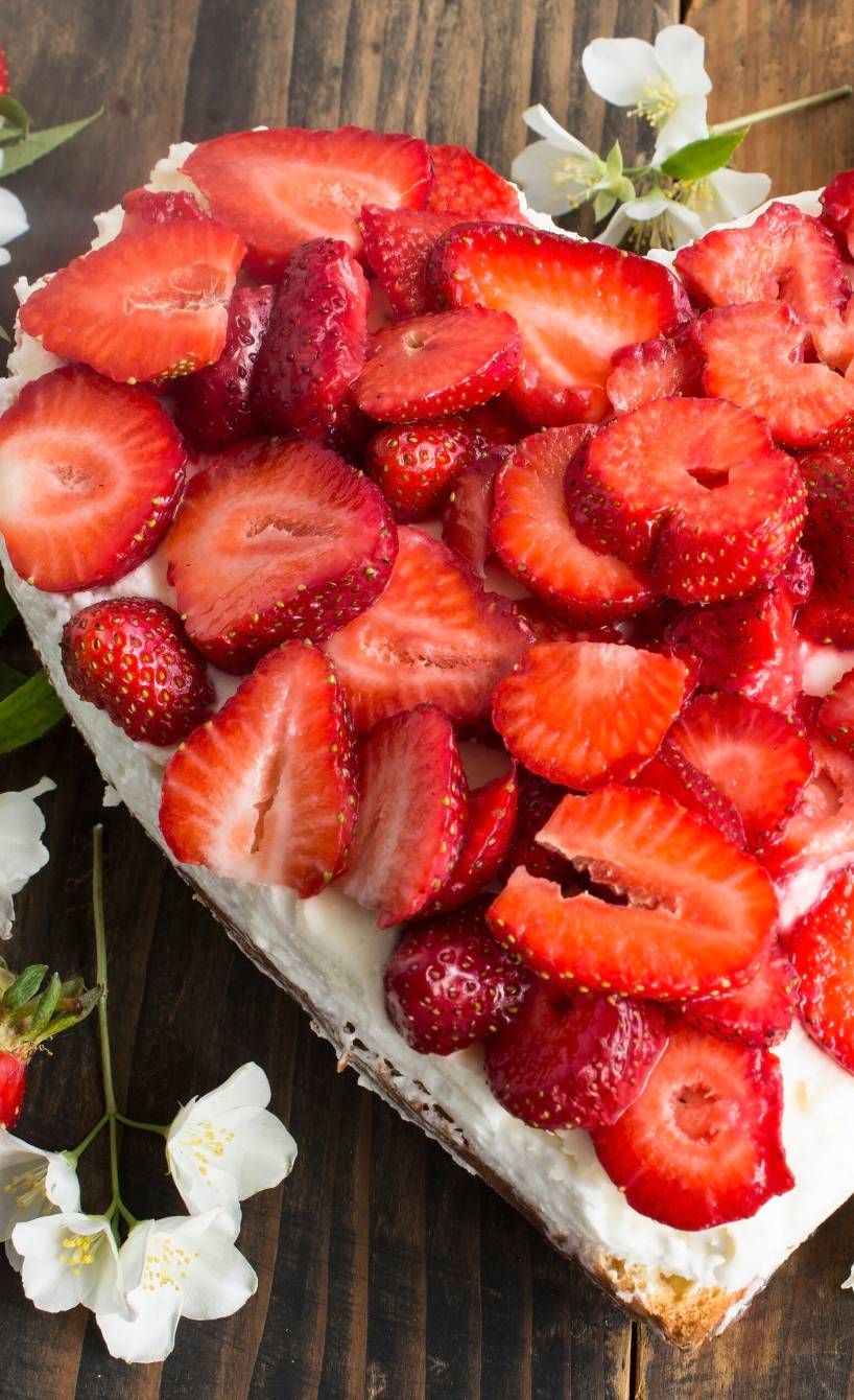 Kleiner Erdbeerkuchen mit Raffaello-Creme in Herzform auf einem Holztisch umgeben von weißen Blüten