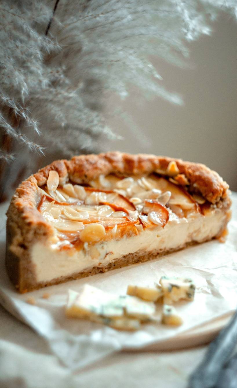Ein halber Gorgonzola-Cheesecake mit Birnen und Mandeln angerichtet auf einer Kuchenplatte