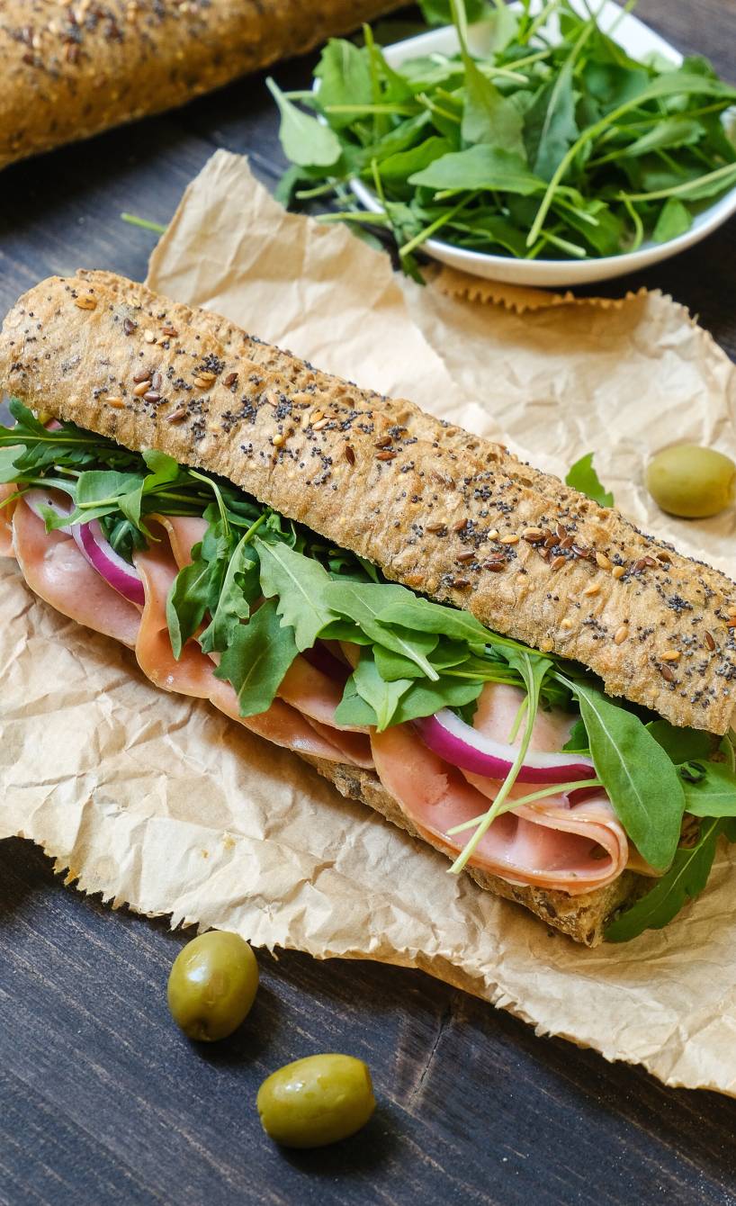 Ein Mortadella-Sandwich mit Rucola und Burrata-Creme auf einem Stück Backpapier auf einem Tisch