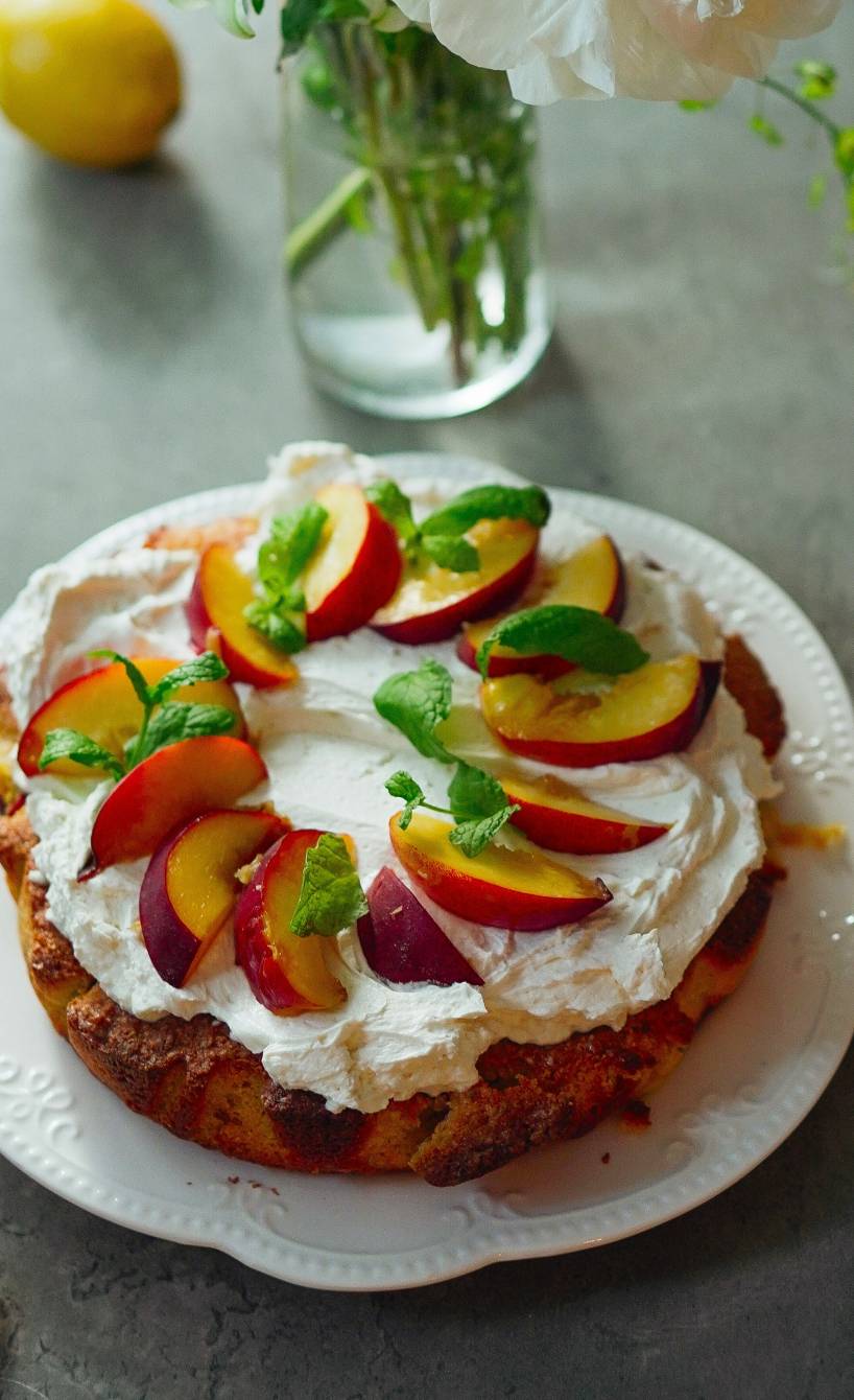 Runder Polenta-Pfirsichkuchen mit Mascarpone-Creme garniert mit frischer Minze auf einer Kuchenplatte