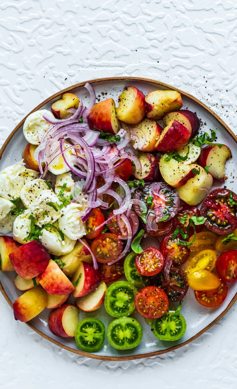Low Carb Tomatensalat mit Plattpfirsich und Mozzarella angerichtet auf einem Teller, daneben Dressing