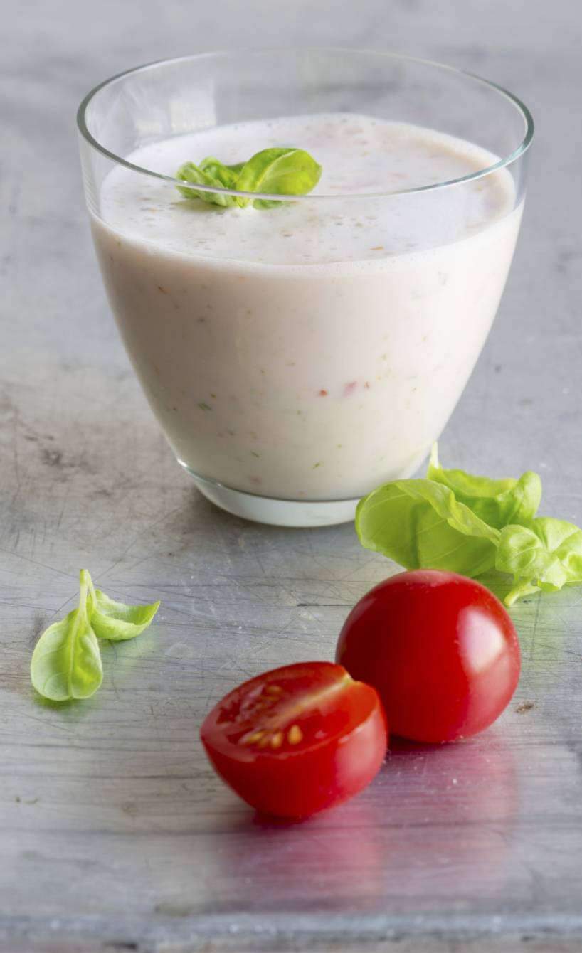 Ein Glas Buttermilch-Tomaten-Drink garniert mit frischem Basilikum in einem Glas auf einem Tisch