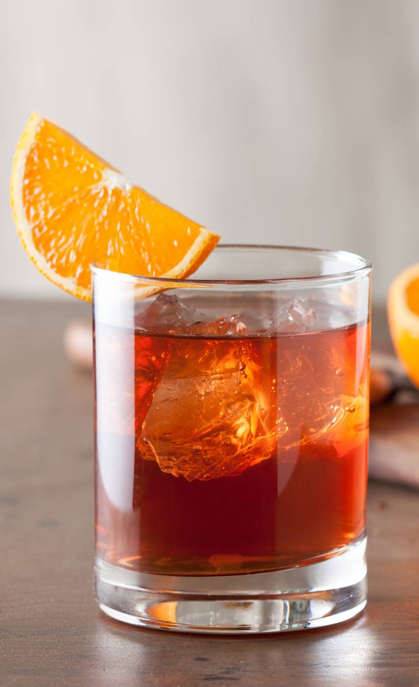 Selbstgemixter Negroni in einem Cocktailglas dekoriert mit einer Orangenscheibe auf einem Tisch
