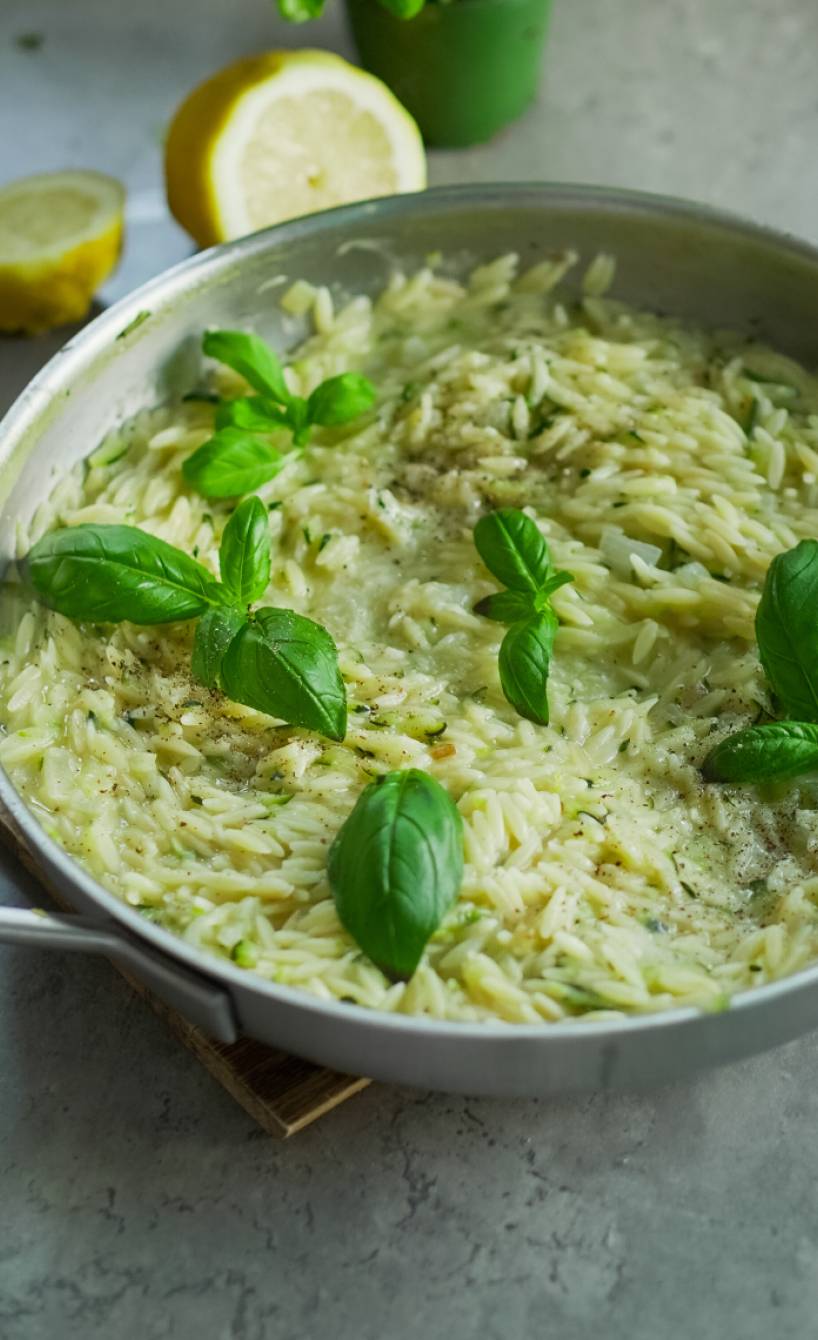 Pfanne mit Orzotto aus Risoni, Zucchini, Zitrone und Parmesan auf einem Tisch