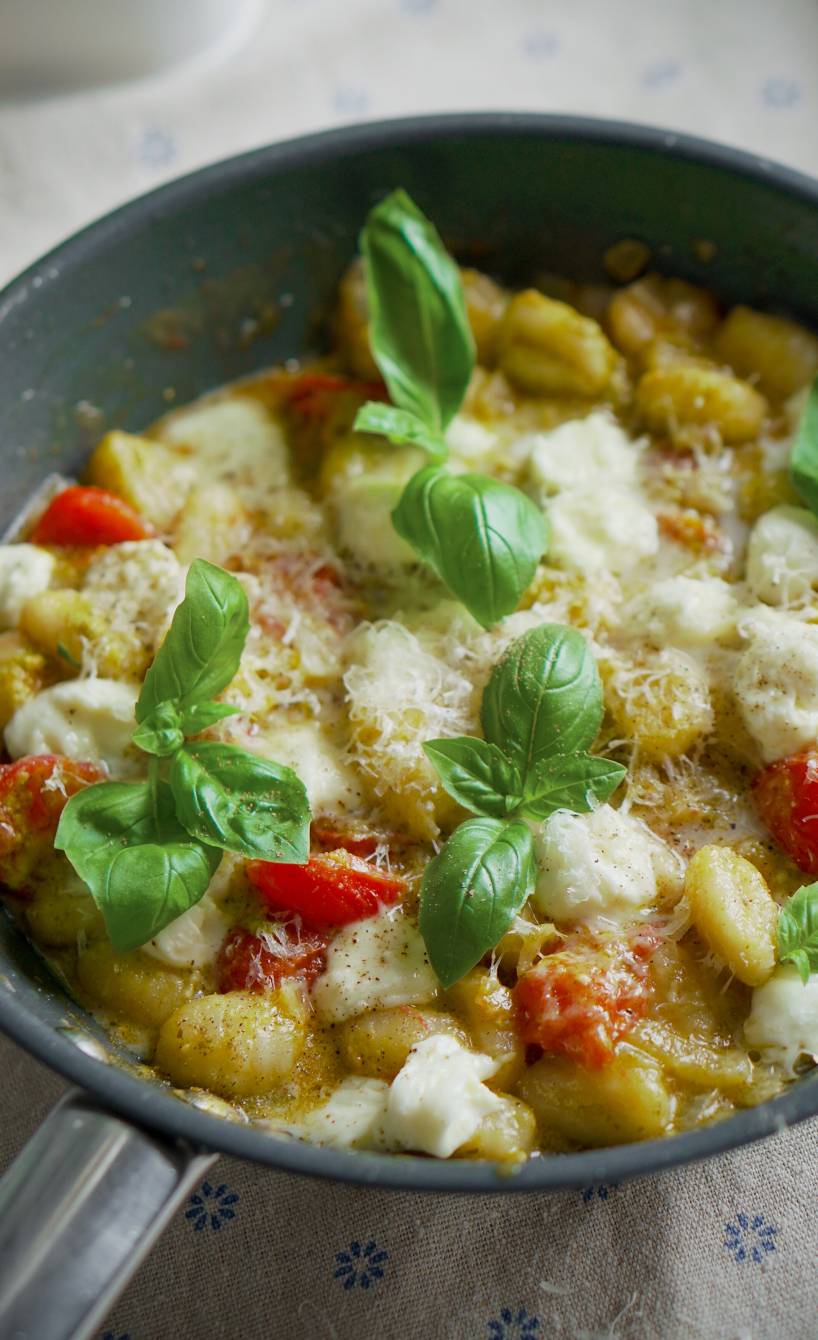 One-Pot Gnocchi mit Tomaten und Mozzarella in einer Pfanne auf einem Tisch garniert von frischem Basilikum