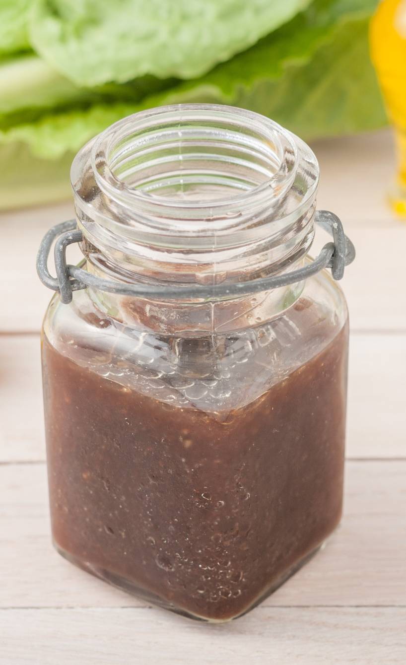 Selbstgemachte Balsamico-Vinaigrette in einem Weckglas auf einem hellen Holztisch neben Salatzutaten