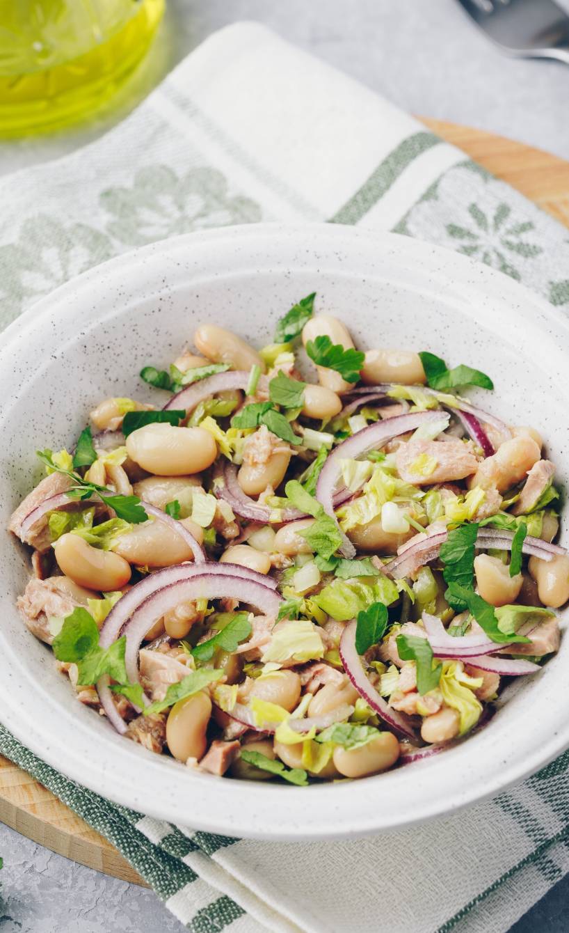 Italienischer Thunfisch-Bohnensalat angerichtet mit roten Zwiebeln auf einem tiefen Teller, daneben Olivenöl