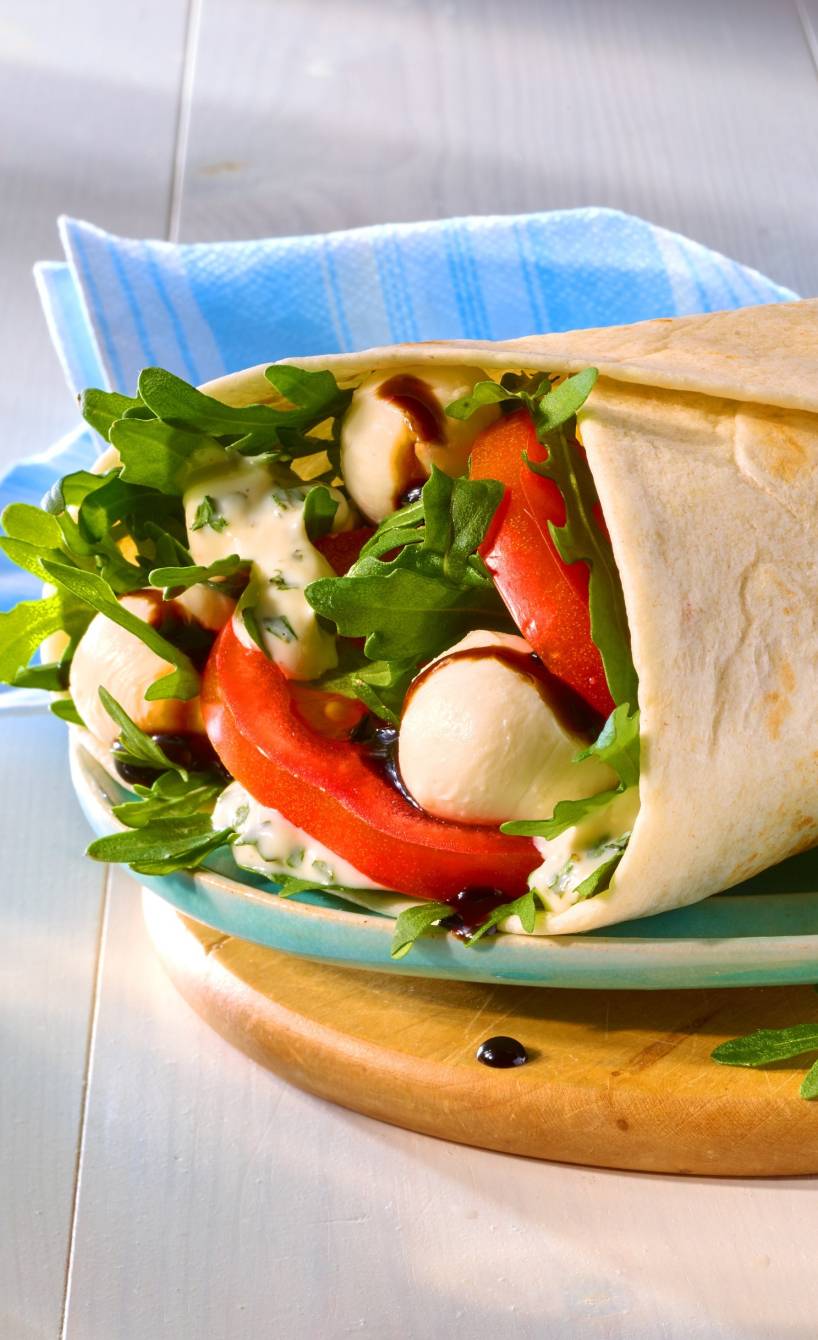 Ein Wrap mit Tomate-Mozzarella-Füllung und Rucola auf einem Teller angerichtet Ein Wrap mit Tomate-Mozzarella-Füllung und Rucola auf einem Teller angerichtet