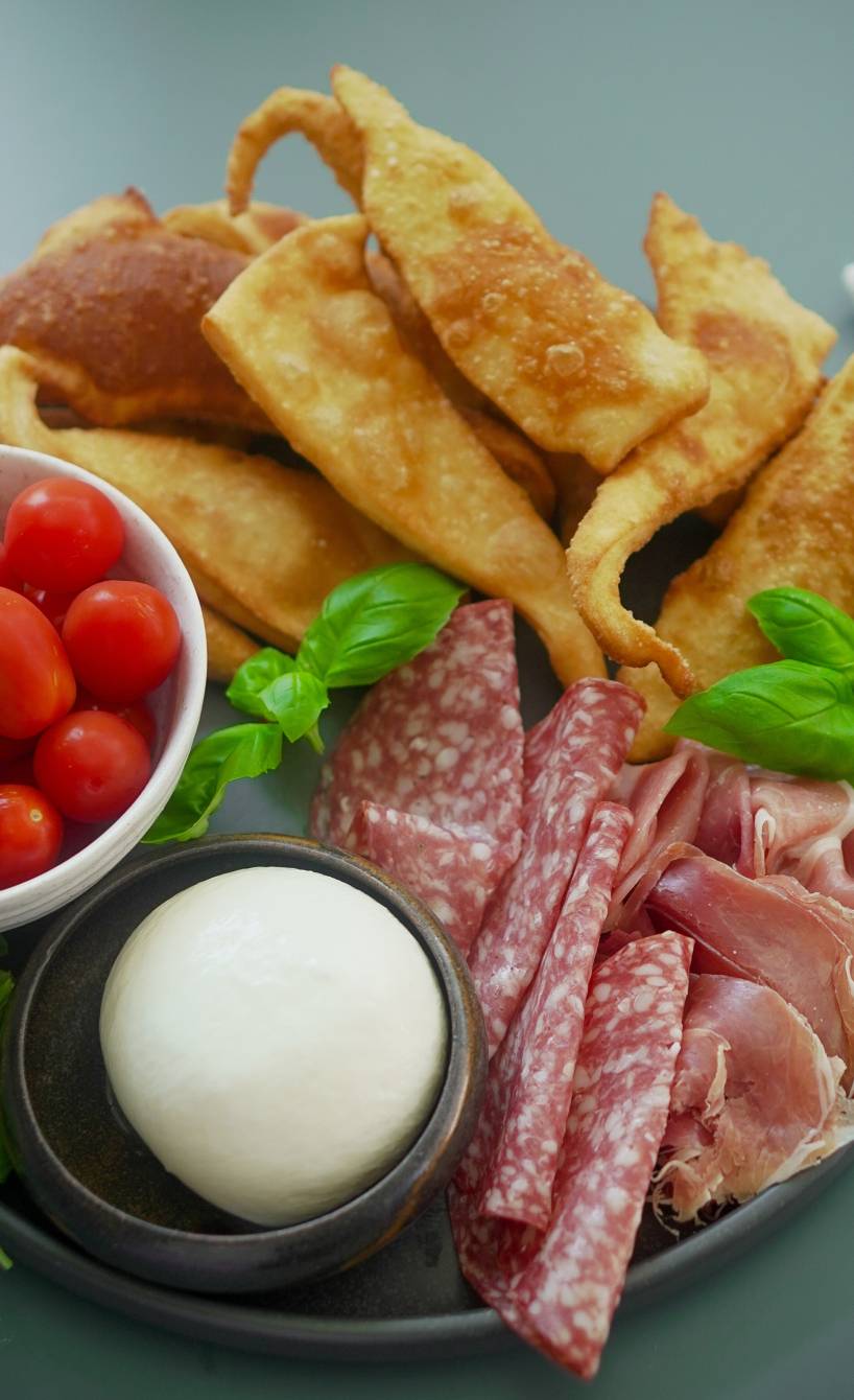 Frittierte Teigkissen Gnocco fritto mit Burrata, Salami, Tomaten und Basilikum angerichtet auf einer Antipasti-Platte