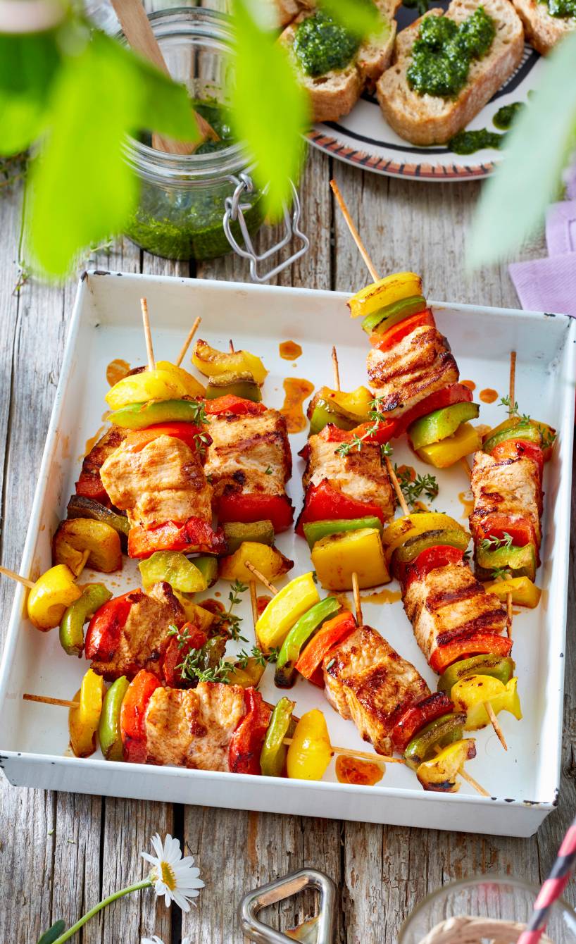 Gegrillte Hähnchen-Paprika-Spieße getoppt mit Basilikumpesto angerichtet auf einer Platte auf einem Gartentisch