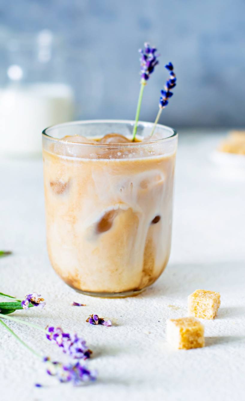Ein Glas selbstgemachte Iced Lavendel Latte dekoriert mit Lavendendelzweigen auf einem Tisch