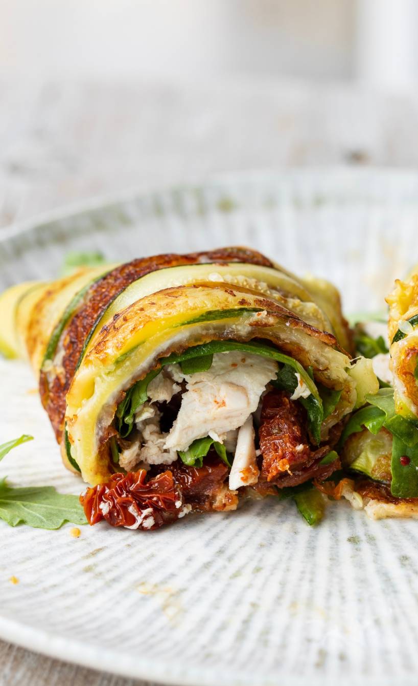 Zwei gerollte Italienische Wraps gefüllt mit Hähnchen, Zucchini und Käse angerichtet auf einem Teller
