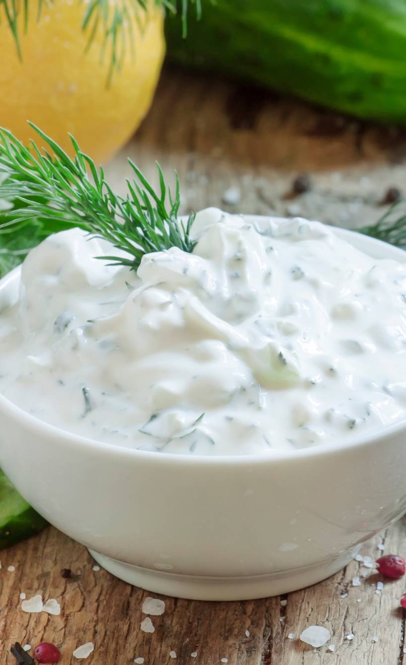 Selbstgemachtes italienisches Joghurtdressing mit frischen Kräutern in einer Schale auf einem Tisch, daneben Salatzutaten