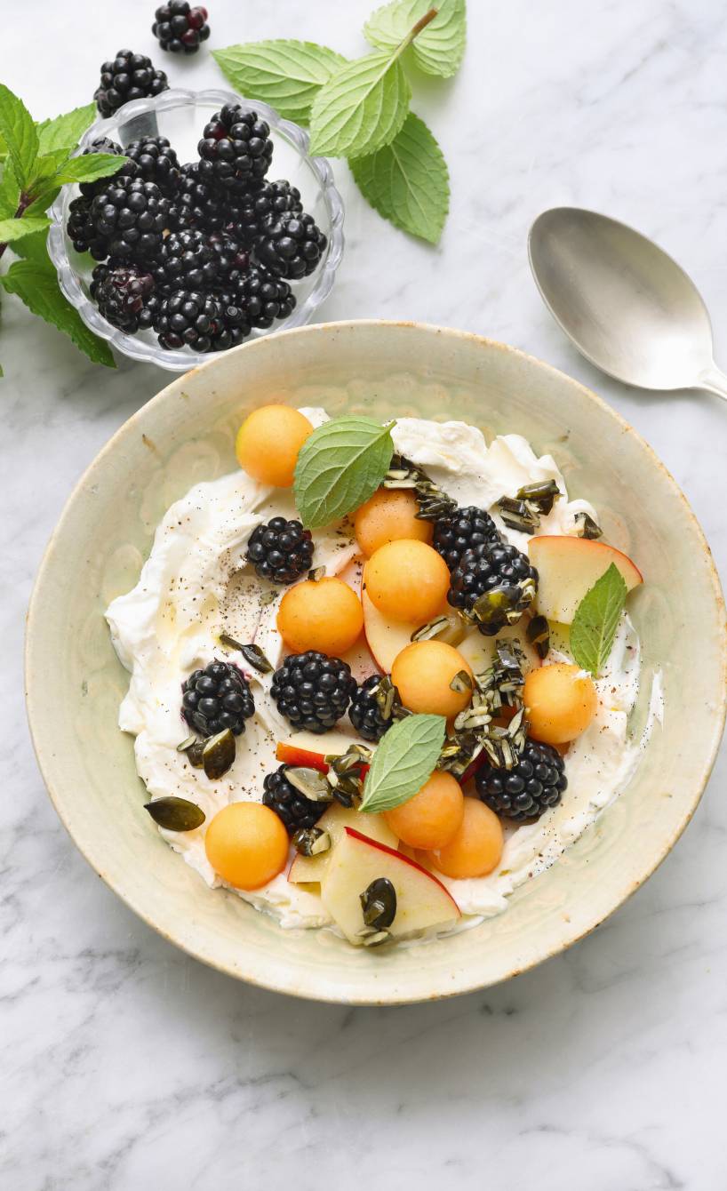 Obstsalat angerichtet auf Mascarpone-Quark-Creme getoppt von Kürbiskernen und Minzblättern auf einem Dessertteller