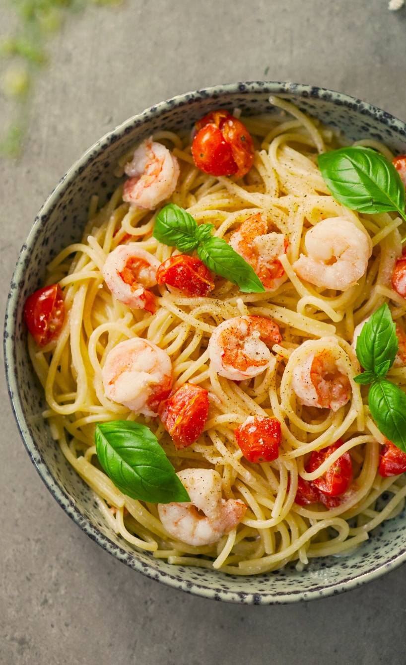 Eine Schale mit One Pot mit Spaghetti, Garnelen, Kirschtomaten und Zitronen-Ricotta garniert mit Basilikumblättern auf einem Tisch