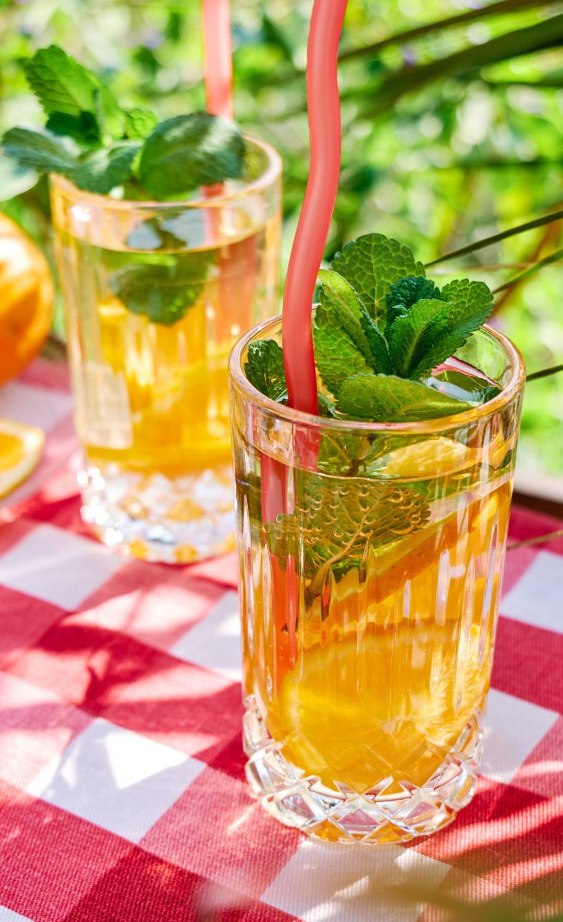 Zwei Gläser selbstgemachter Orangen-Minz-Eistee auf einem Gartentisch