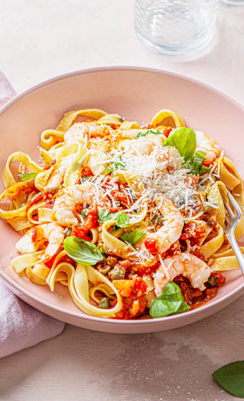 Tagliatelle alla puttanesca mit Knoblauchgarnelen angerichtet auf einem Pastateller