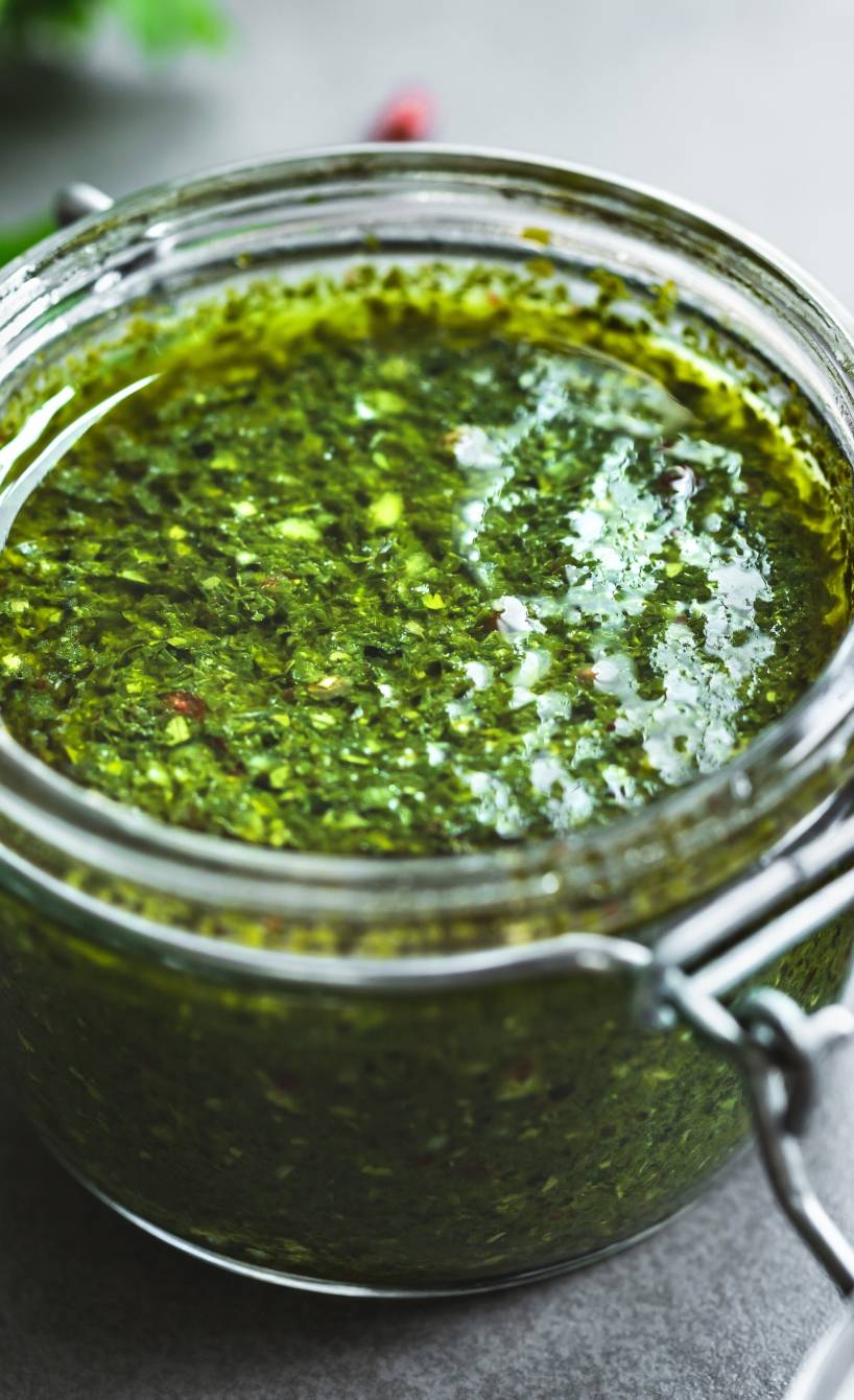 Selbstgemachtes Kräuterdressing Salsa Verde in einem Bügelglas auf einem Tisch, daneben Zutaten wie Knoblauch und Kräuter