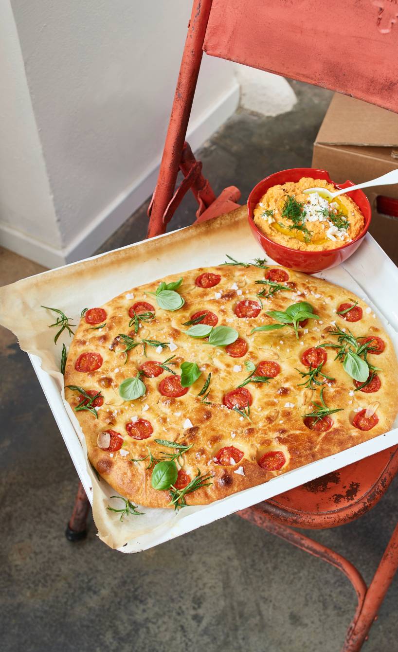 Selbstgebackene Tomaten-Focaccia auf einem Backblech, daneben eine Schale mit Feta-Dip