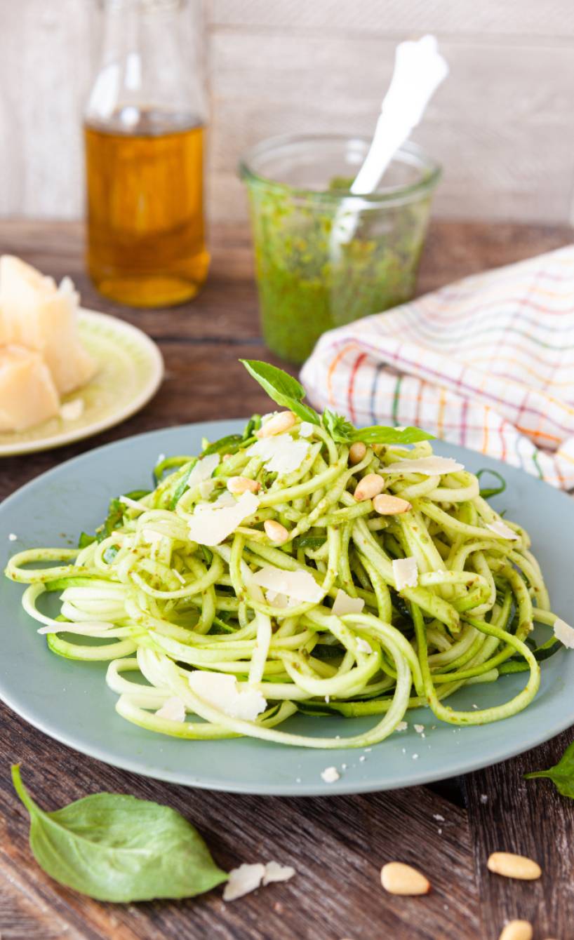 Zucchini-Nudeln mit Zucchini-Pesto angerichtet auf einem Pastateller mit Parmesan und Pinienkernen