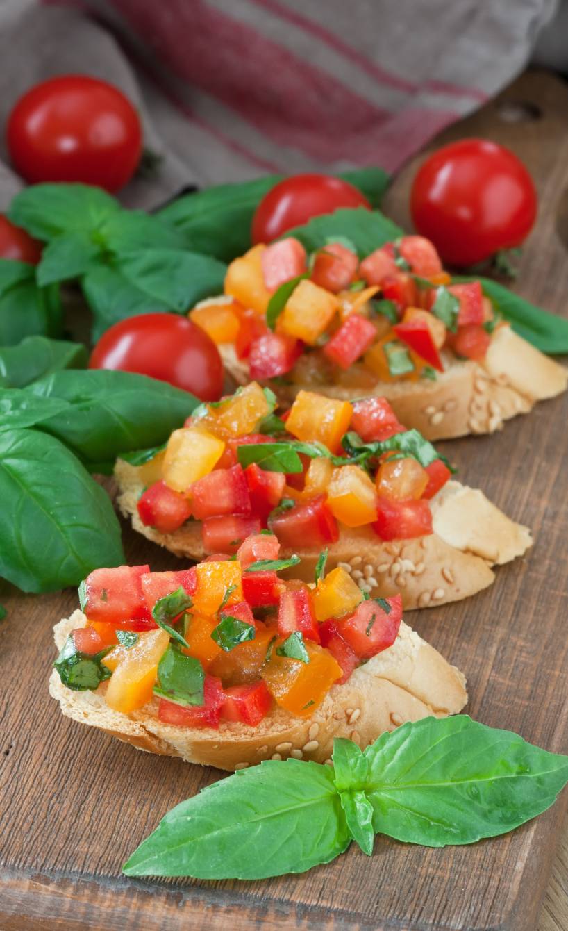 Bruschetta mit gelben und roten Datterini, Basilikum und Olivenöl angerichtet von Serena Loddo auf einem Holzbrett