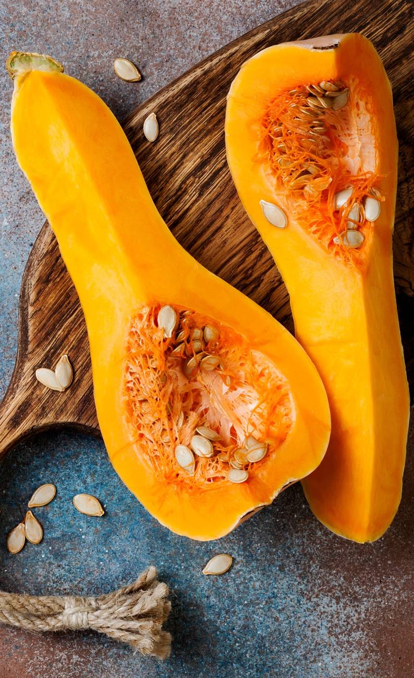 Ein aufgeschnittener Butternut Kürbis liegt ungeschält auf einem Tisch und einem Holzbrett