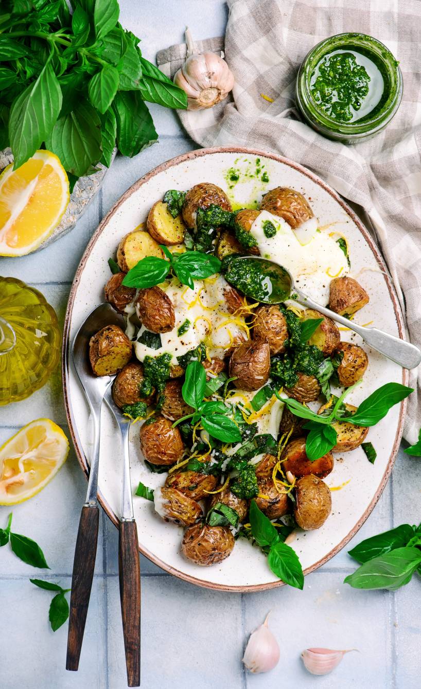 im Backofen gebackene Drillinge mit Burrata und grünem Pesto angerichtet auf einer Servierplatte getoppt von Zitronenabrieb und Basilikumblättern 