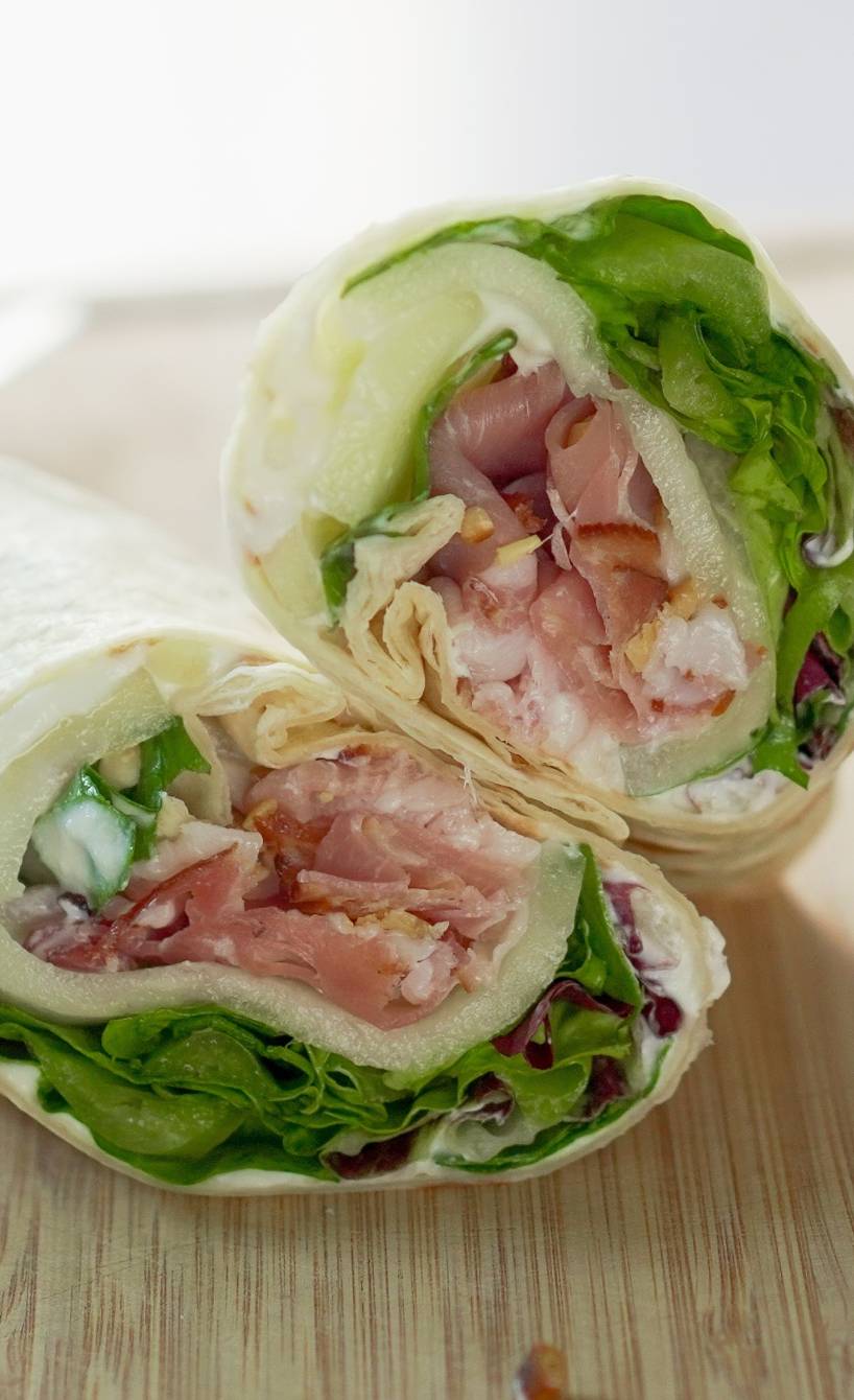 Halbierter Schinken-Melone-Wrap auf einem Holzbrett Halbierter Schinken-Melone-Wrap auf einem Holzbrett