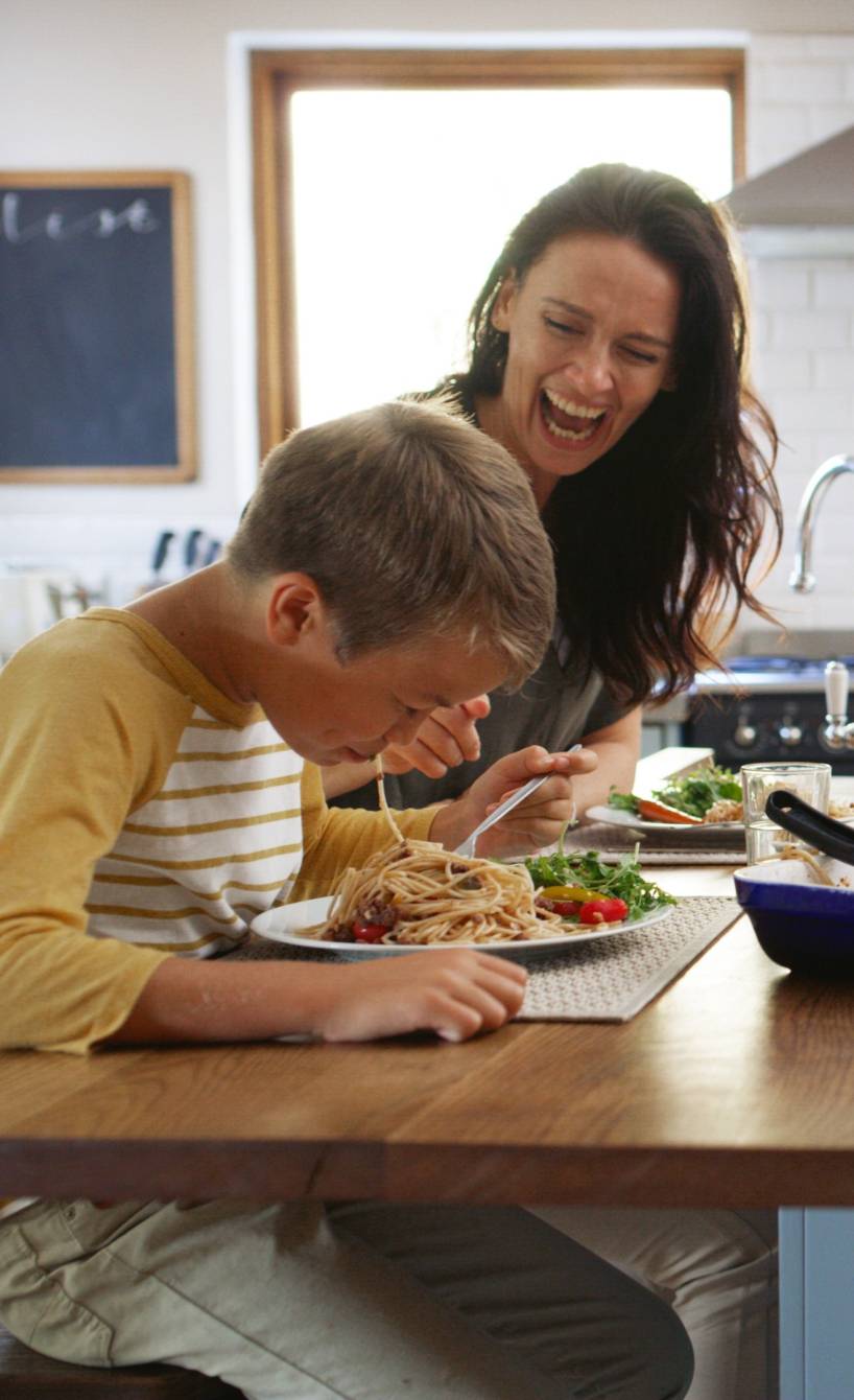 Eine vierköpfige Familie sitzt beim Abendessen an einer Kücheninsel und genießt Spaghetti