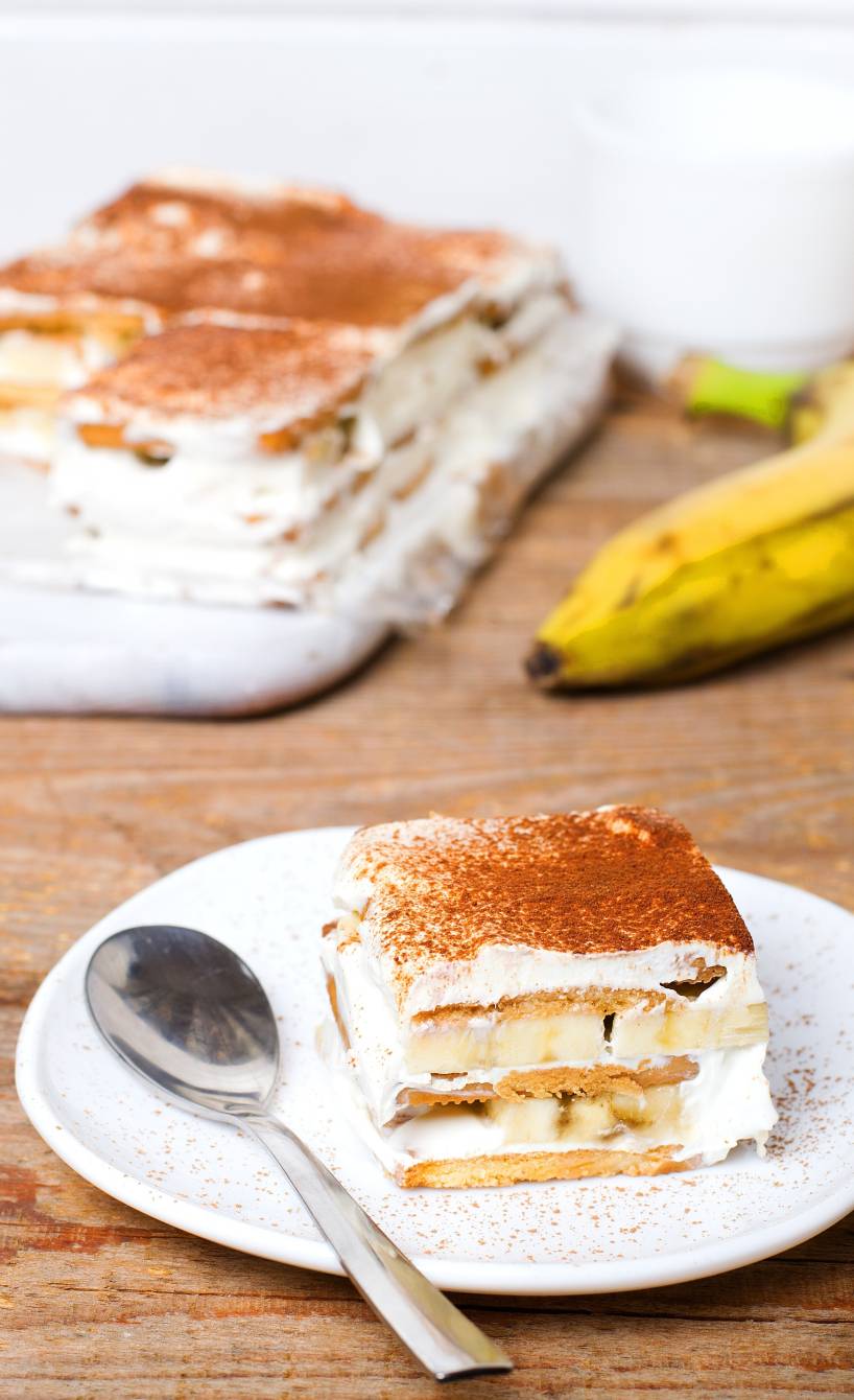 Ein Stück Schoko-Bananen-Tiramisu auf einem Dessertteller, daneben frische Bananende