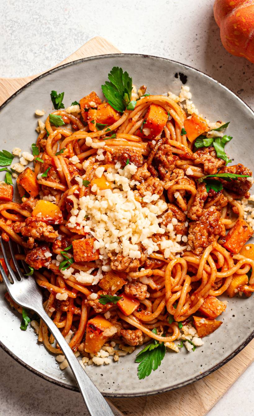 Spaghetti mit Kürbis-Hackfleisch-Bolognese angerichtet auf einem Pastateller getoppt von geriebenem Parmesan auf einem Esstisch
